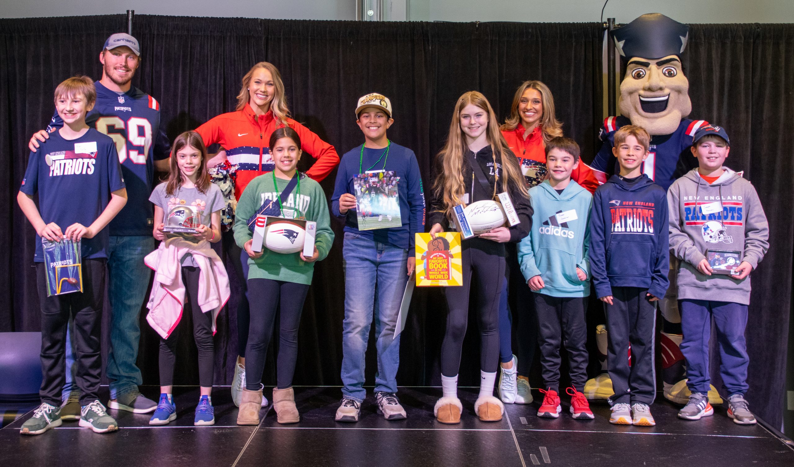Smiling students pose with their challenge prizes standing with Patriots cheerleaders and mascot